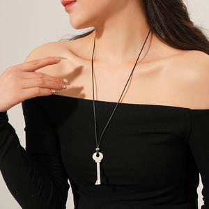 Gros plan d'un pendentif clé argenté minimaliste sur un long collier en cordon noir