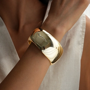 Close-up of a wide polished gold metal cuff bracelet on a model's wrist with mirror finish