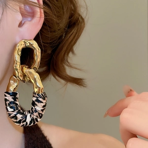 Detail of geometric metal earrings with animal print texture worn on model ear