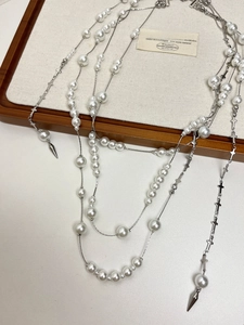 Detail of layered silver necklace with pearls, cross pendants, and conical charms on a tray