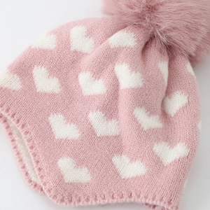 Gros plan du bonnet tricoté rose pour bébé avec motifs cœurs et pompon doux en peluche