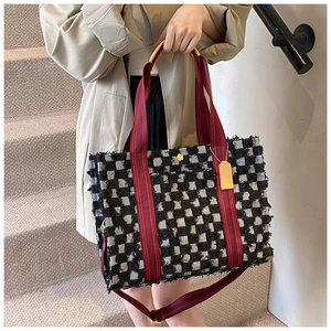Close-up of black and white checkered tweed tote bag with red strap and fringe detail