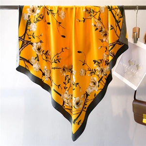 Foulard carré en soie jaune avec imprimé magnolia et bordure noire sur un cintre