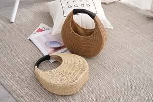 Handwoven straw handbags in beige and light brown with black handles on a woven rug
