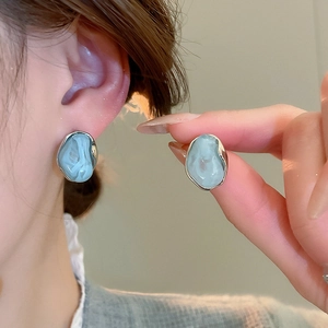 Dettaglio di orecchini in resina marmorizzata blu con bordi argentati su modella e mano