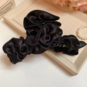 Detail view of a large black satin bow hair claw clip with pleated texture on a tray