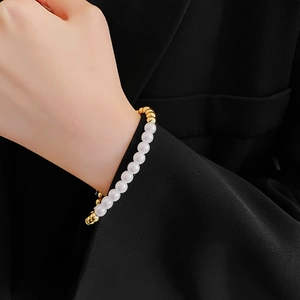 Dettaglio dell'elegante bracciale di perle bianche con sfere dorate su una giacca nera