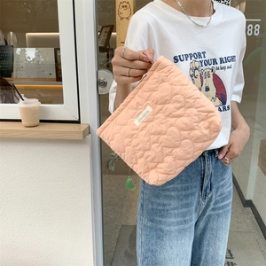 Pink quilted pouch with heart pattern being held by a model in a cozy cafe setting