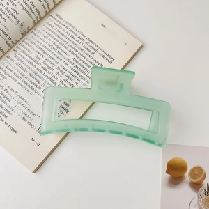 Détail d'une pince à cheveux mate vert clair avec design rectangulaire creux et citrons