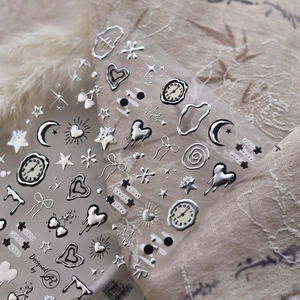 Silver metallic 3D nail stickers featuring 3D hearts, stars and moons on a beige fabric