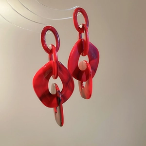 Detail of red marble texture acrylic earrings with geometric link chain design on stand