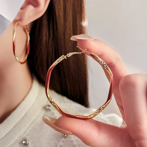 Detail of large gold hoop earrings with wavy texture and reddish brown enamel finish