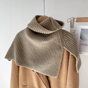 Detail of beige ribbed knit turtleneck poncho layered over a camel wool coat