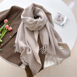Detail of beige cashmere-feel knit scarf with fringes and minimalist woven label