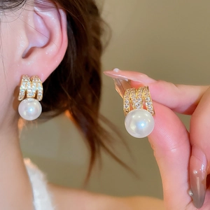 Detail of gold M-shaped earrings with sparkling cubic zirconia and hanging white pearl
