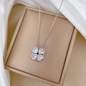 Detailed view of silver four-leaf clover necklace with crystals in a beige jewelry box