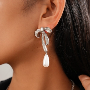 Détail de boucles d'oreilles nœud argenté avec strass brillants et perles gouttes