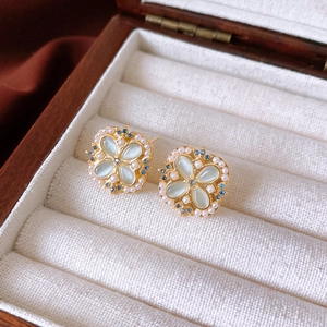Close-up of gold clover earrings with green cat-eye stone and pearls in a jewelry box