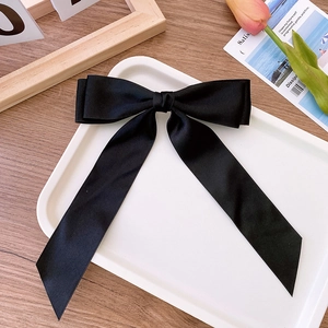 Detail of elegant black satin double bow hair clip on a white tray with tulip decor