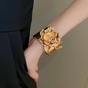 Detail of a large 3D golden rose sculpture on a metallic wide cuff bangle bracelet