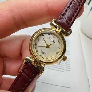 Close-up of quartz watch with silver dial, gold case, and brown leather strap