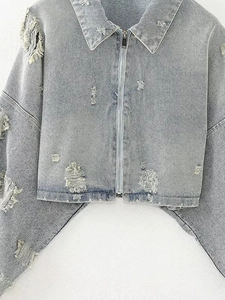 Detail of light blue distressed denim jacket featuring ripped edges and high-quality texture