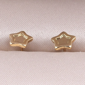 Macro shot of gold star-shaped stud earrings on soft pink silk texture background