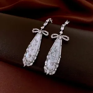 Silver bow water drop earrings with shimmering crystals on premium silk background