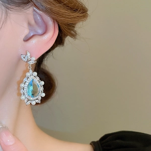 Close-up of blue teardrop gemstone earring with pearls and diamond bow knot on model