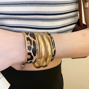 Close-up of leopard print cuff bracelets and gold bangles set worn on wrist