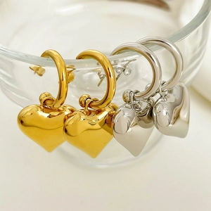 Polished gold and silver heart dangle hoop earrings displayed on a glass rim