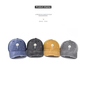 Detail of washed denim baseball caps with daisy embroidery and distressed ripped finish