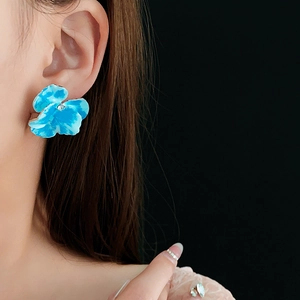 Dettaglio di un orecchino a fiore in smalto blu con diamante sull'orecchio della modella