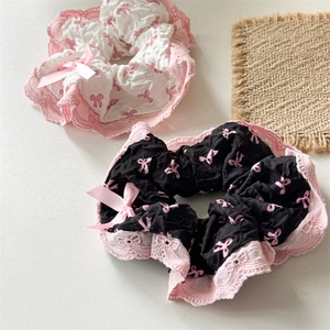 Close-up of black and white lace scrunchies with pink bow prints on a neutral background