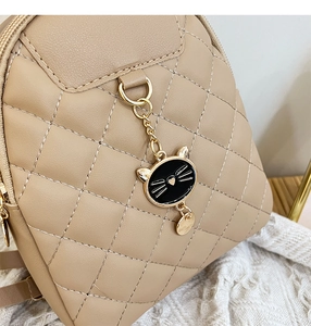 Detail of beige quilted backpack featuring a cute black cat charm and gold zipper