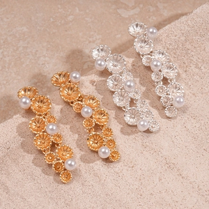 Detail of layered metal flower earrings with pearls on a textured stone surface