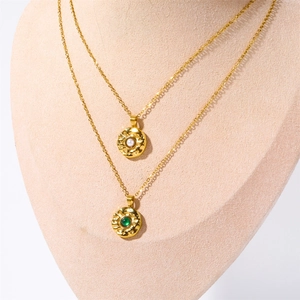 Double layered gold necklace with white pearl and green gemstone on hammered pendants