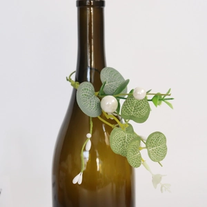 Détail d'un rond de serviette eucalyptus et baies de perles blanches sur une bouteille