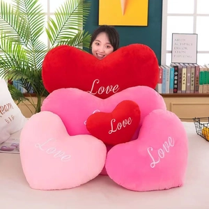 Detail of soft heart plush pillows in red and pink with Love embroidery on a bed