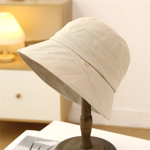 Chic beige bucket hat for women with minimalist metal logo on a stylish wood stand