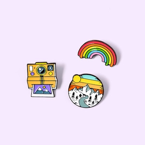 Set of 3 cartoon enamel pins featuring yellow camera, rainbow, and sunset landscape designs