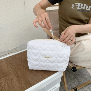 Close-up of white heart-quilted toiletry bag with zipper opening in an outdoor setting