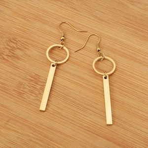 Detailed view of golden geometric long bar earrings with circular ring on wood background
