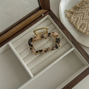 Macro view of a square leopard print claw clip in a velvet lined wooden box