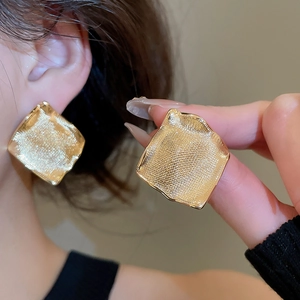 Vue détaillée de boucles d'oreilles carrées dorées avec texture martelée sur modèle et main