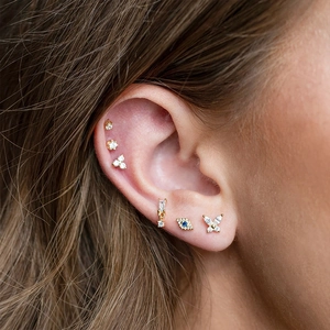 Detail of female model wearing gold ear studs with zircon butterflies and eye motifs