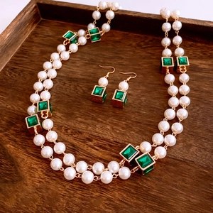 Detail view of double-layer pearl necklace and emerald earrings on a wooden tray