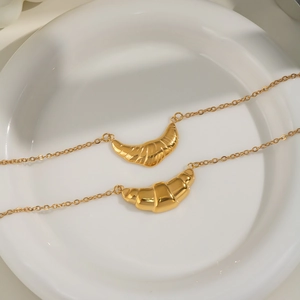 Gold croissant pendant necklace on white ceramic plate with warm minimalist aesthetic
