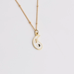 Close-up of gold-plated paisley pendant with white enamel and Tai Chi yin yang symbol
