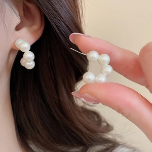 Macro shot of elegant C-shaped acrylic pearl stud earrings worn on ear with golden needle